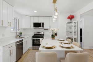 Kitchen featuring an eat-at island with pendant lighting, white cabinetry with gold-tone hardware, stainless steel appliances, and wood-finish flooring