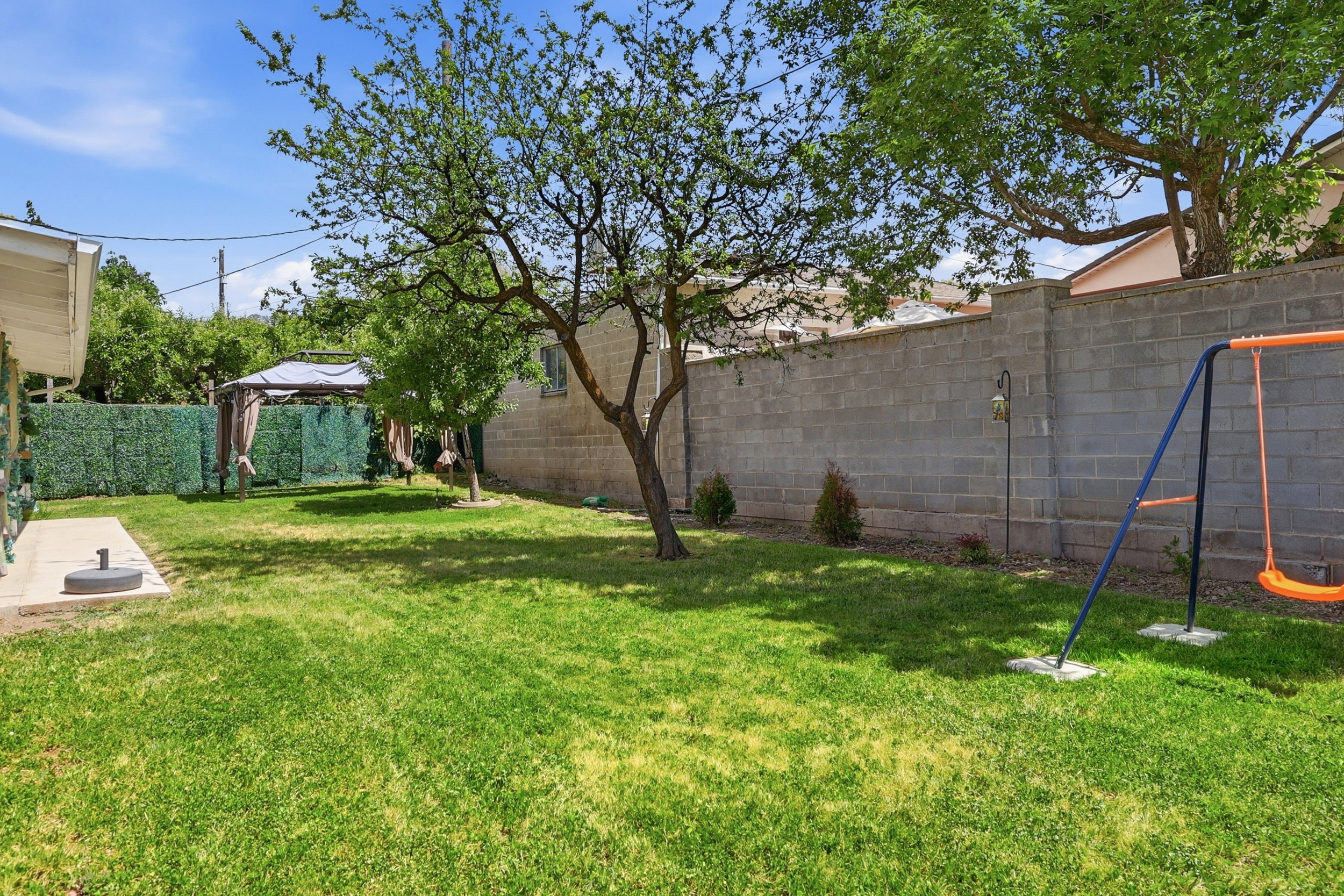 Expansive backyard featuring a lush lawn, mature shade trees, a concrete block privacy wall, and a paved patio area
