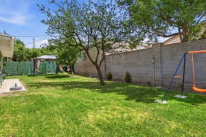 Expansive backyard featuring a lush lawn, mature shade trees, a concrete block privacy wall, and a paved patio area