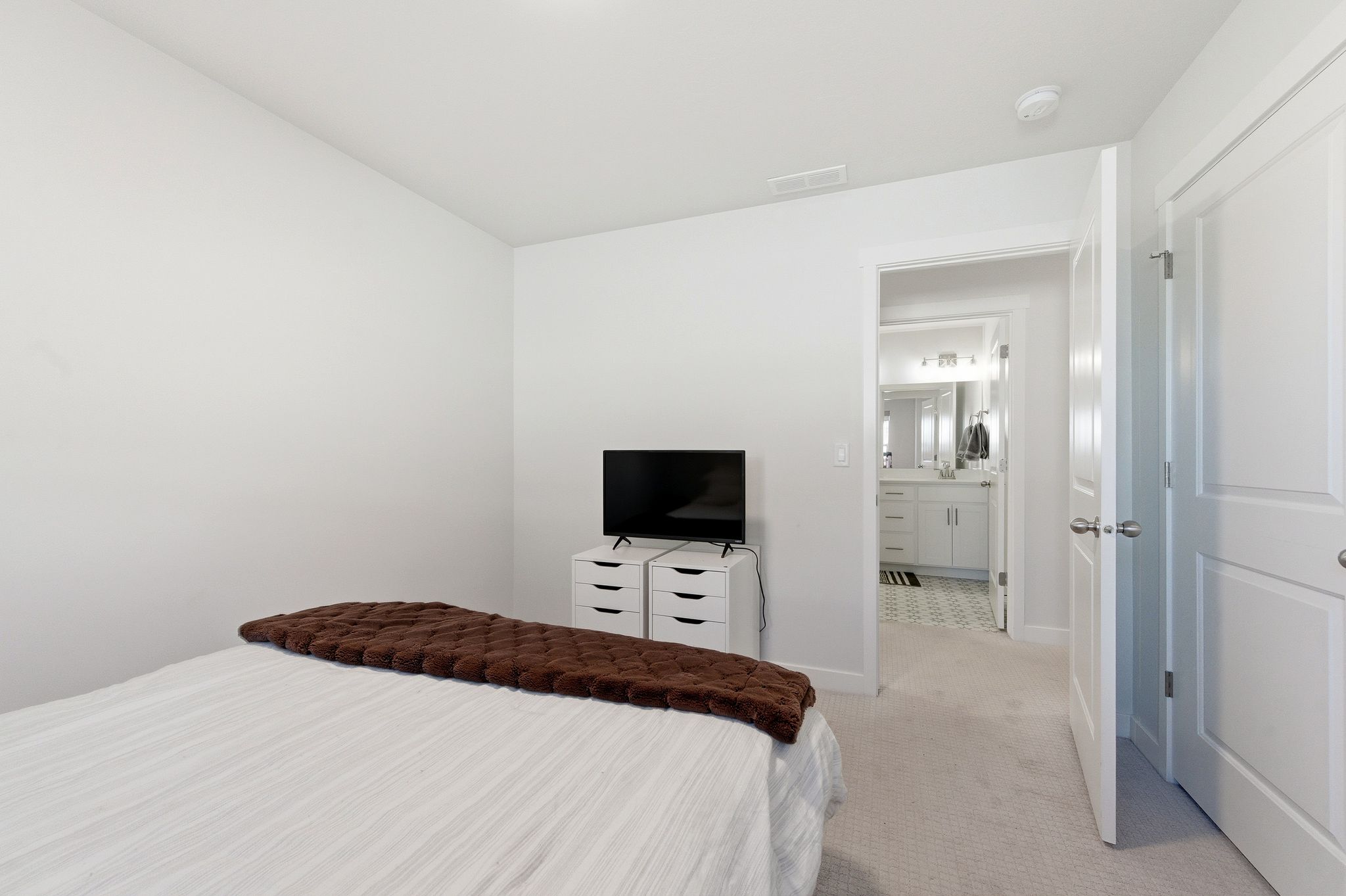 Bedroom space featuring light-toned carpeting and a door opening to a bathroom