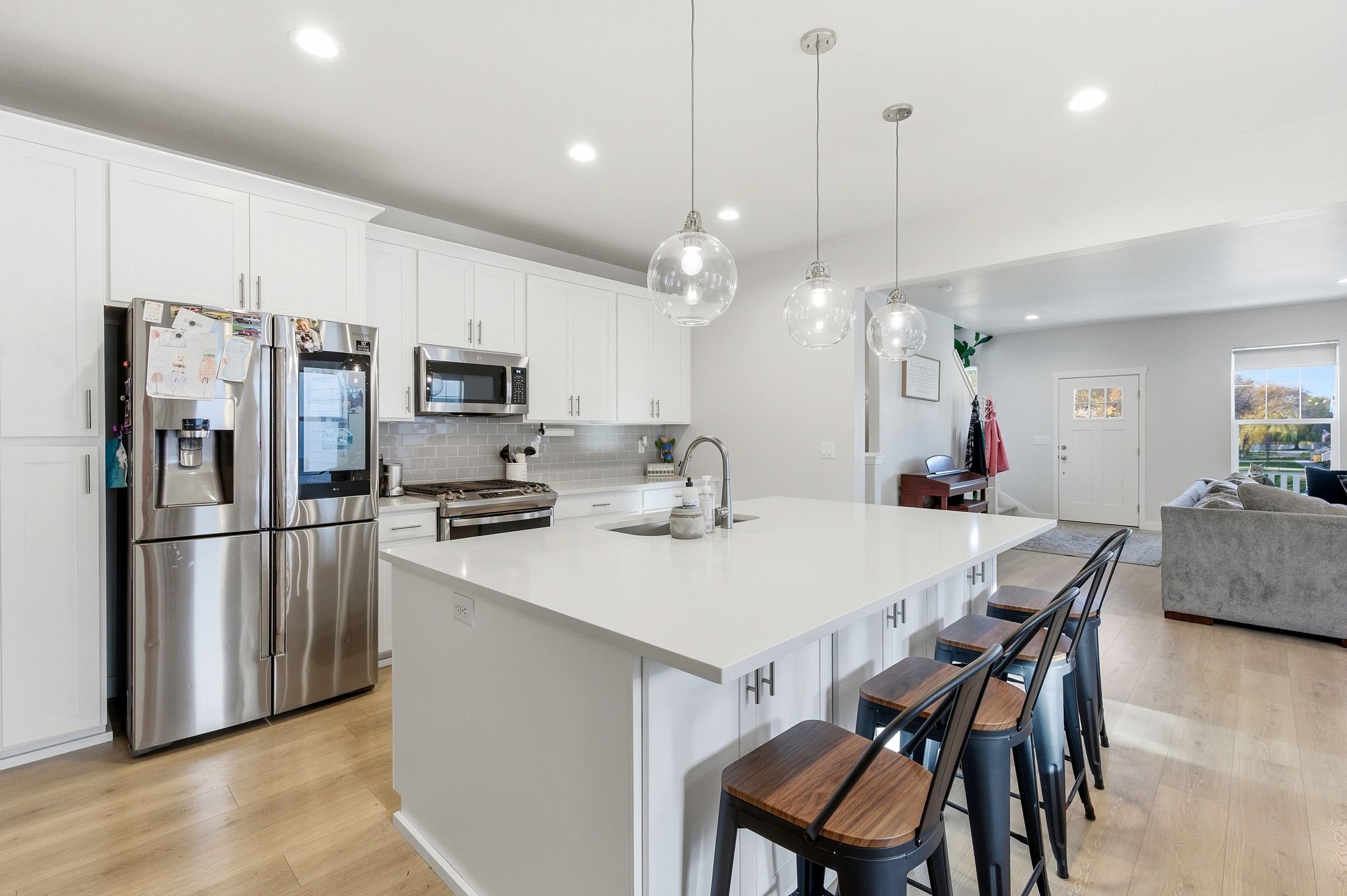 Contemporary kitchen featuring an expansive island with seating, white shaker cabinetry, stainless steel appliances, and wood-finish flooring