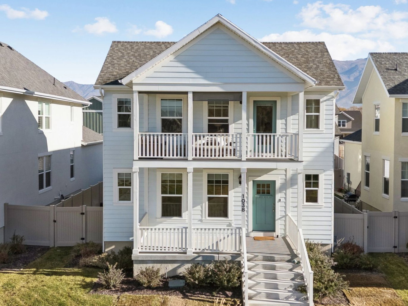 Two-story light blue siding residence featuring a covered front porch and an upper-level balcony with white railings