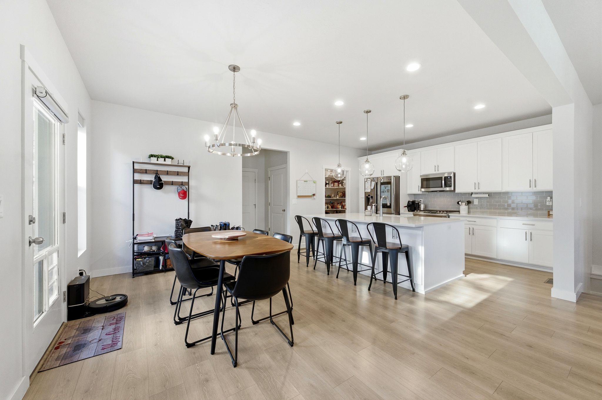 Open-concept living space featuring wood-finish flooring, a modern white kitchen with an island and stainless steel appliances, recessed lighting, and a dining area illuminated by a contemporary chandelier