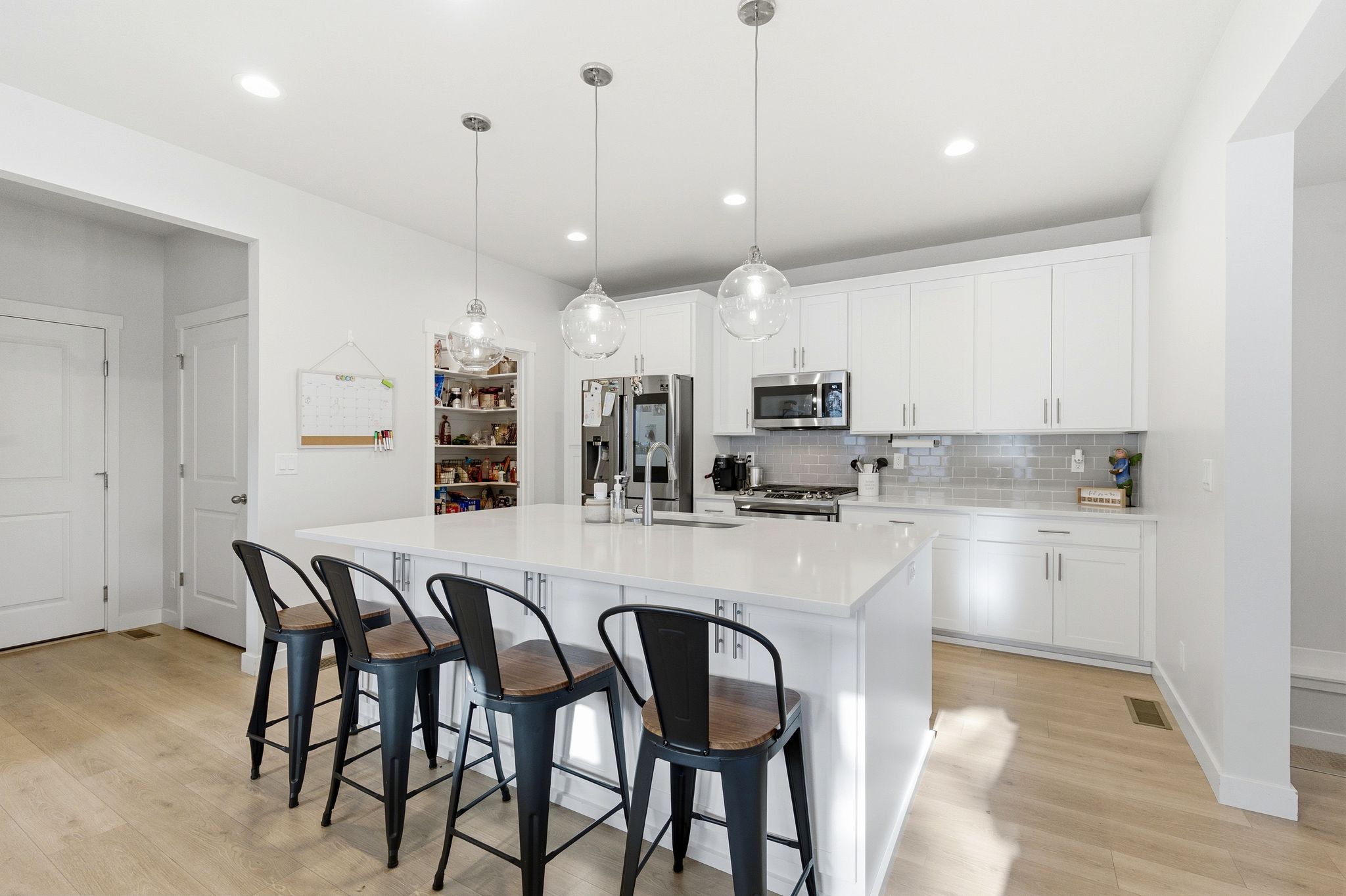 Modern kitchen featuring a large central island with seating for four, white cabinetry, integrated stainless steel appliances, a subway tile backsplash, and light wood-finish flooring