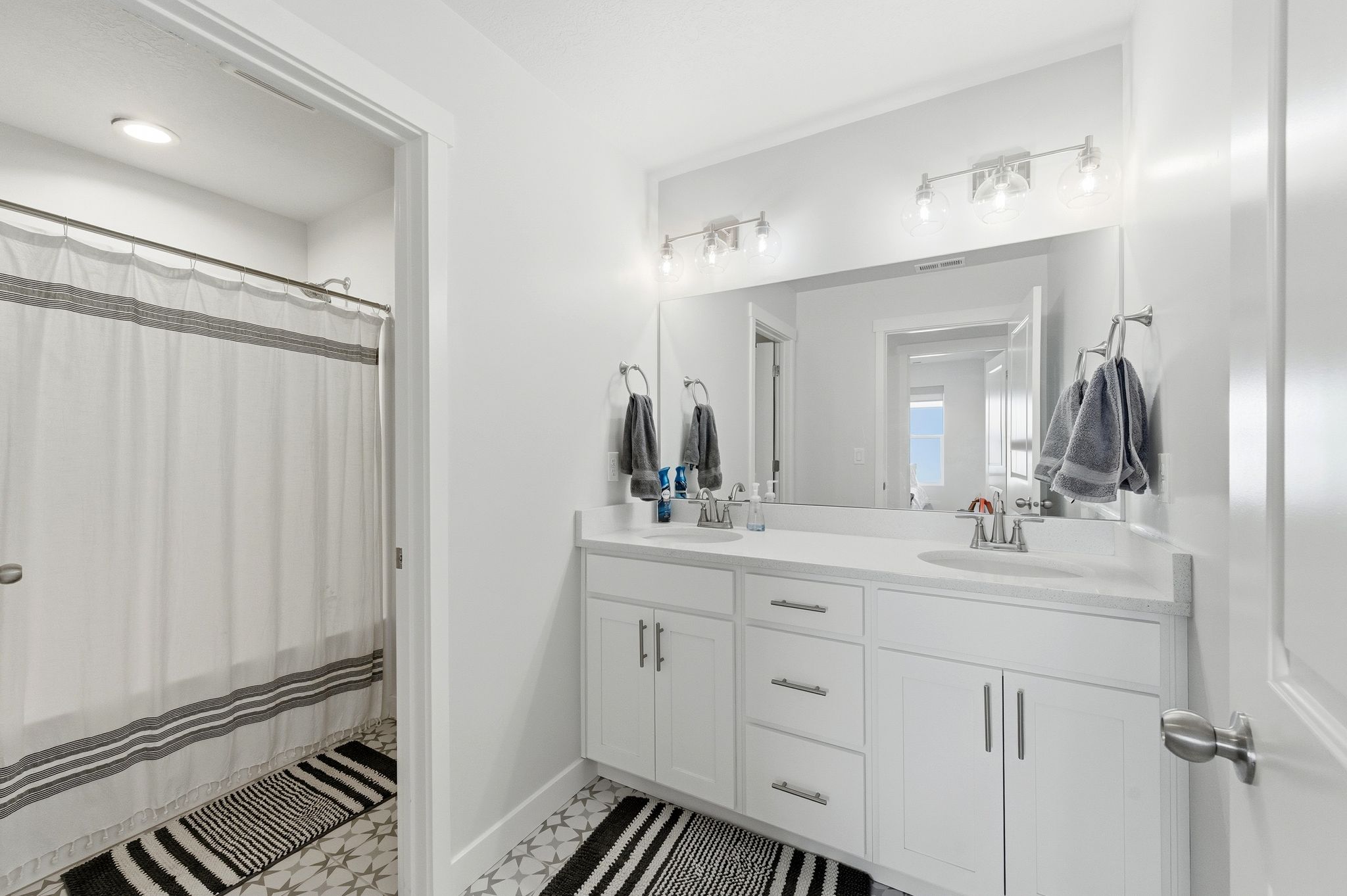 Bathroom featuring a dual vanity with white cabinetry, integrated sinks, and a large wall-mounted mirror