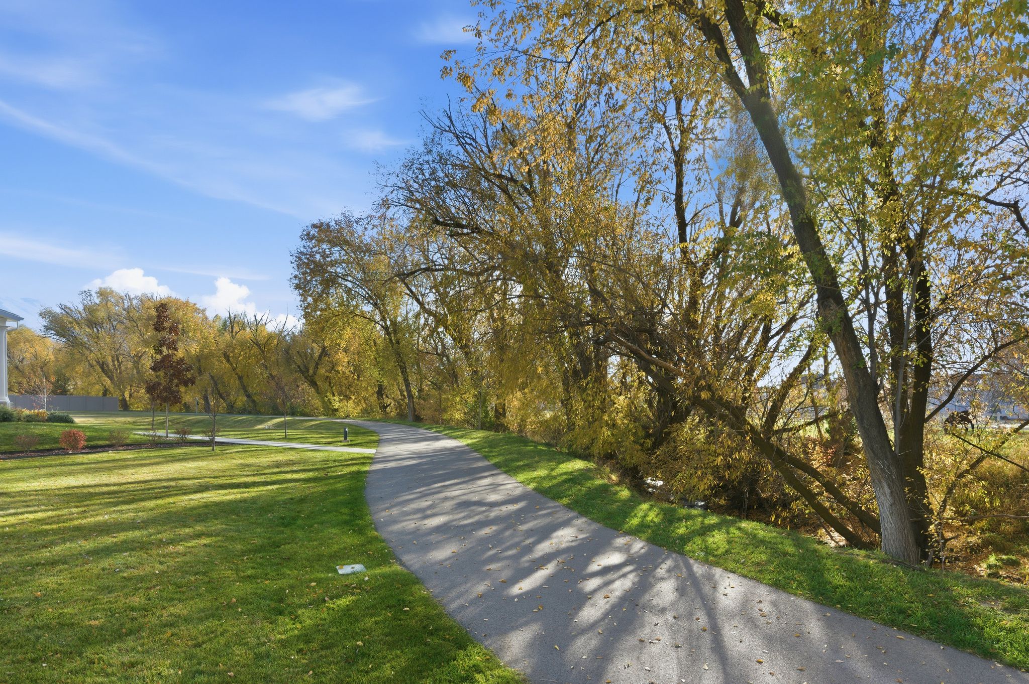 Paved pathway bordered by manicured lawn and mature trees with autumn foliage