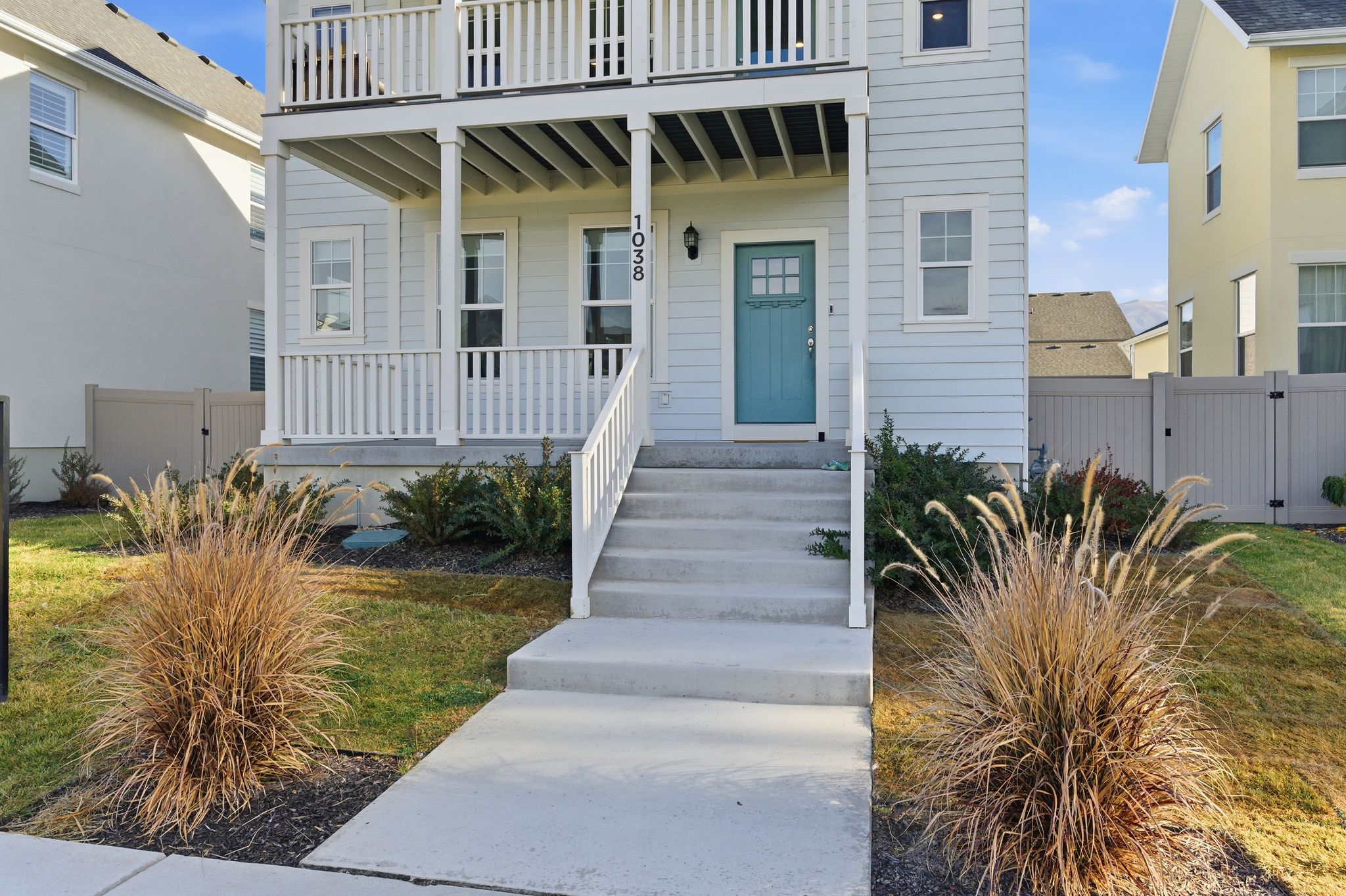 Light blue siding exterior featuring multiple balconies with white railings, a turquoise front door, and a concrete pathway leading to the entrance