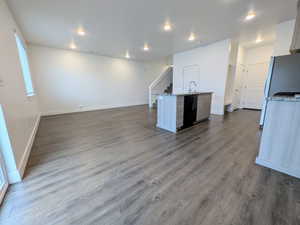Open-concept living space featuring wood-finish flooring, recessed lighting, a central kitchen island with a built-in sink, and granite countertops