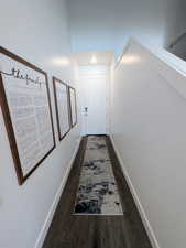 Hallway featuring wood-finish flooring, crisp white baseboards, and a white paneled door with contemporary hardware