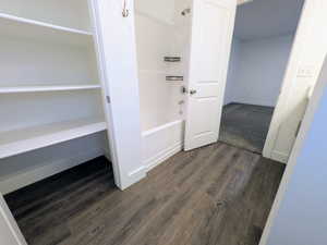 Bathroom featuring wood-finish flooring, a white built-in bathtub with shower, and an adjacent storage closet with multiple shelves