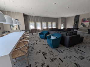 Spacious common area featuring recessed lighting, a long communal table with individual pendant lights, and large windows with full-length drapery
