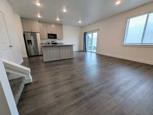 Open-concept living area featuring wood-finish flooring, a kitchen island with granite countertop, stainless steel appliances, and a sliding glass door leading to an exterior space