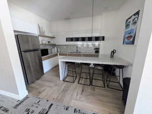 Modern kitchen with an integrated breakfast bar, stainless steel refrigerator, white and wood-finish cabinetry, and light-toned, speckled countertops and backsplash