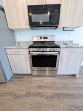 Stainless steel range with a built-in microwave, light wood-finish cabinetry, and granite-style countertops