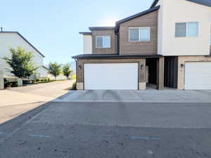 Contemporary townhome exterior featuring a two-car garage, wood-finish siding, light-toned stone accents, and a covered entry