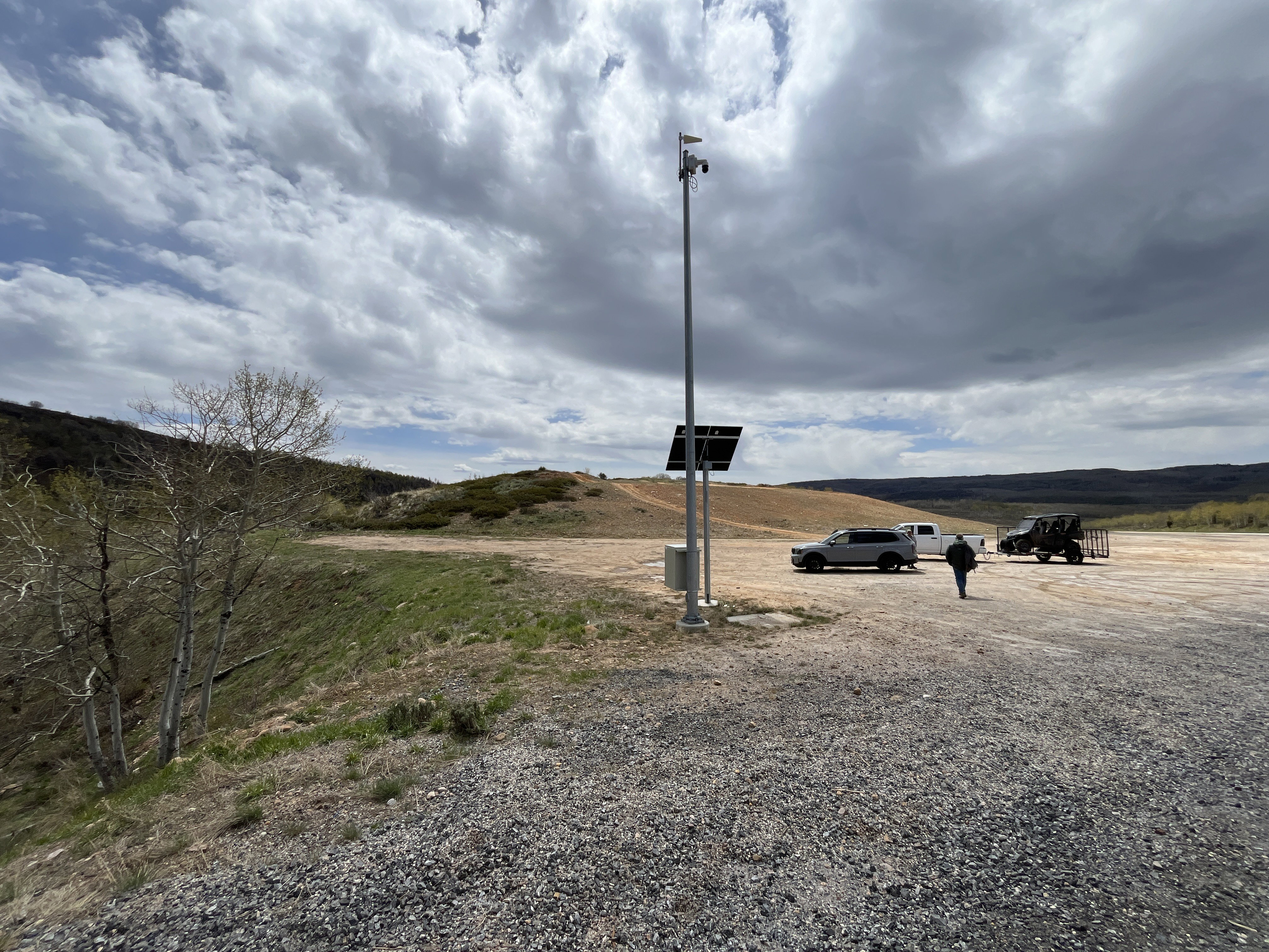 Expansive graveled lot featuring a tall utility pole with solar panels and multiple mounted cameras