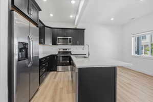 Modern kitchen featuring dark cabinetry, stainless steel appliances, light-toned countertops, and wood-finish flooring