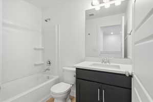 Bathroom featuring a dark wood-finish vanity with a white countertop and undermount sink, a large wall-mounted mirror, and a white tub/shower combination with chrome fixtures