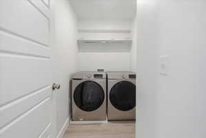 Dedicated laundry area featuring modern front-load appliances, overhead shelving, and wood-finish flooring
