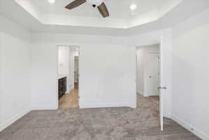 Spacious room featuring tray ceilings, a ceiling fan with wood-finish blades, recessed lighting, and plush grey carpeting