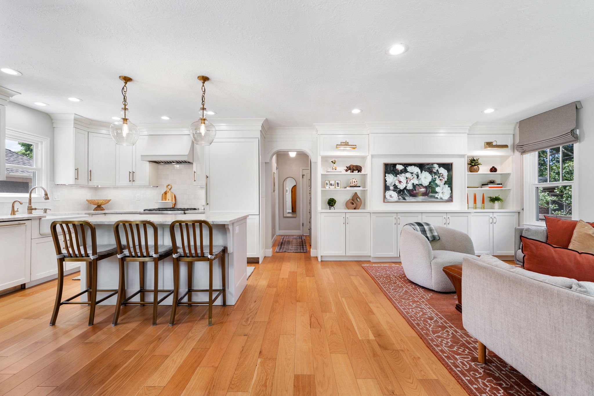 Open-concept living space featuring wood-finish flooring, a kitchen island with seating, white cabinetry, recessed lighting, and built-in shelving with lower storage