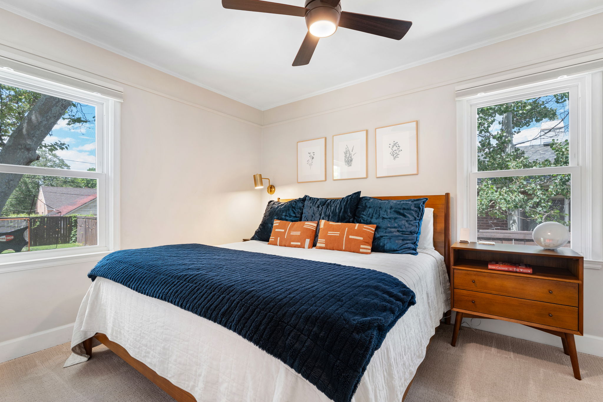 Bedroom featuring two large windows, a ceiling fan with integrated lighting, wall-mounted sconce lighting, and crown molding