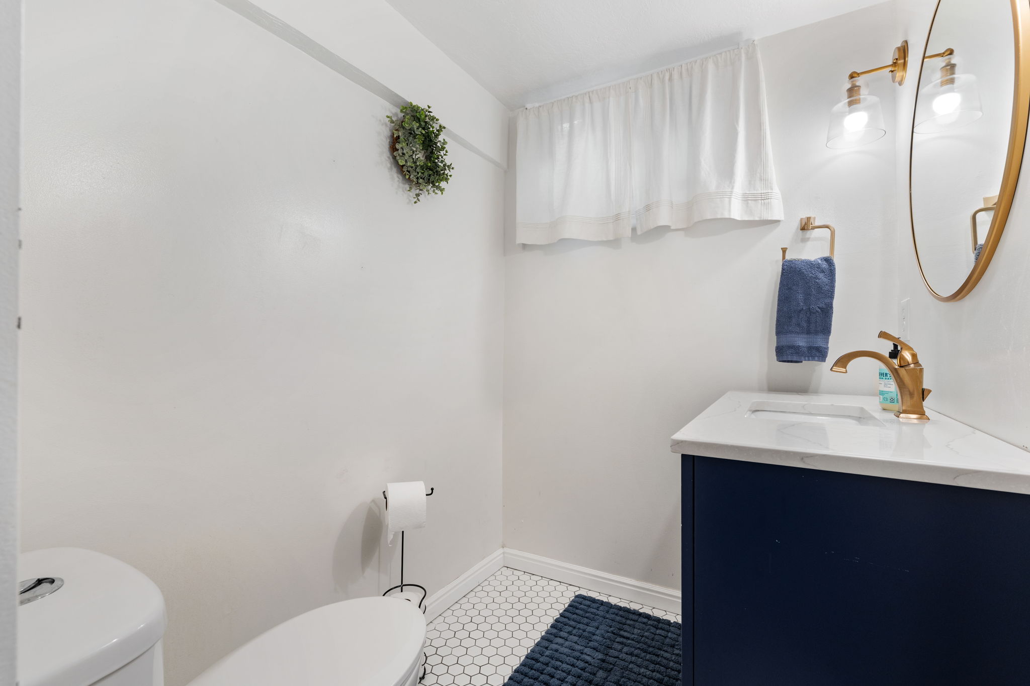 Bathroom featuring a navy blue vanity with a white countertop, gold-finish faucet, and a round gold-frame mirror