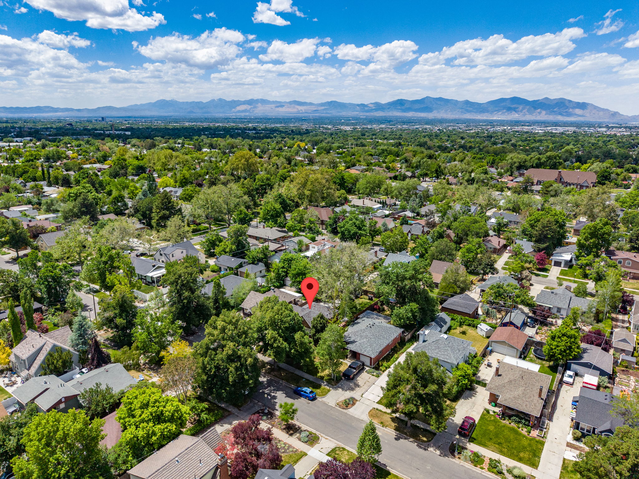 Aerial perspective showcasing the property within a neighborhood characterized by mature trees and residential structures, with distant mountains forming a natural backdrop