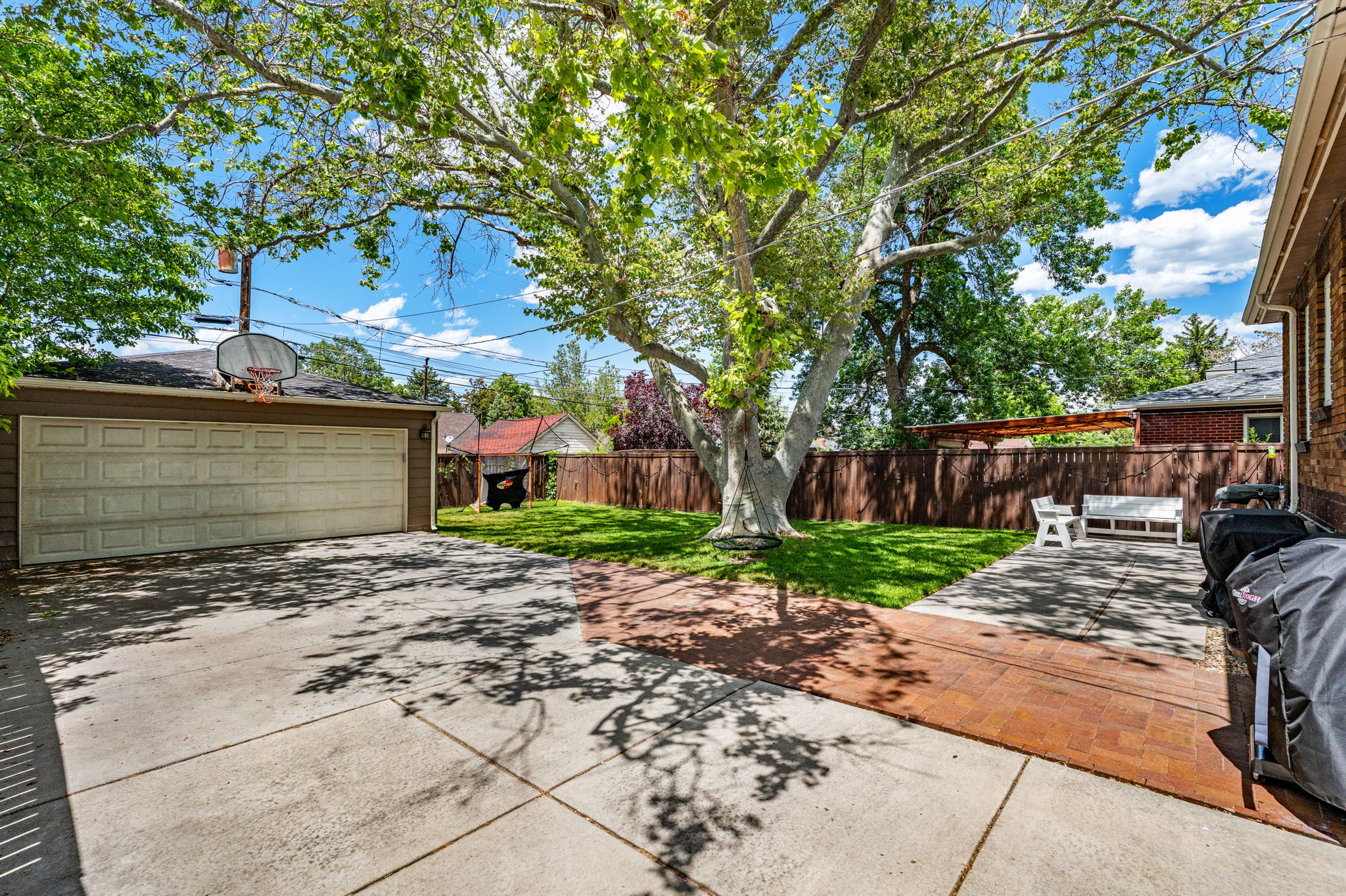 Expansive concrete driveway with a detached two-car garage, brick paver patio, and mature shade trees
