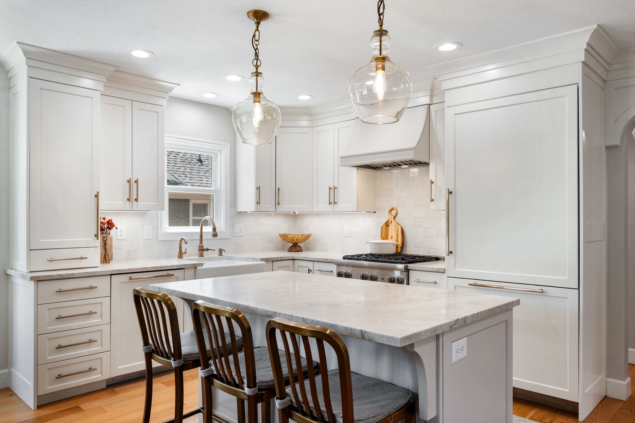 White kitchen cabinetry with crown molding, a central island featuring a stone countertop, a farmhouse sink, and stainless steel appliances
