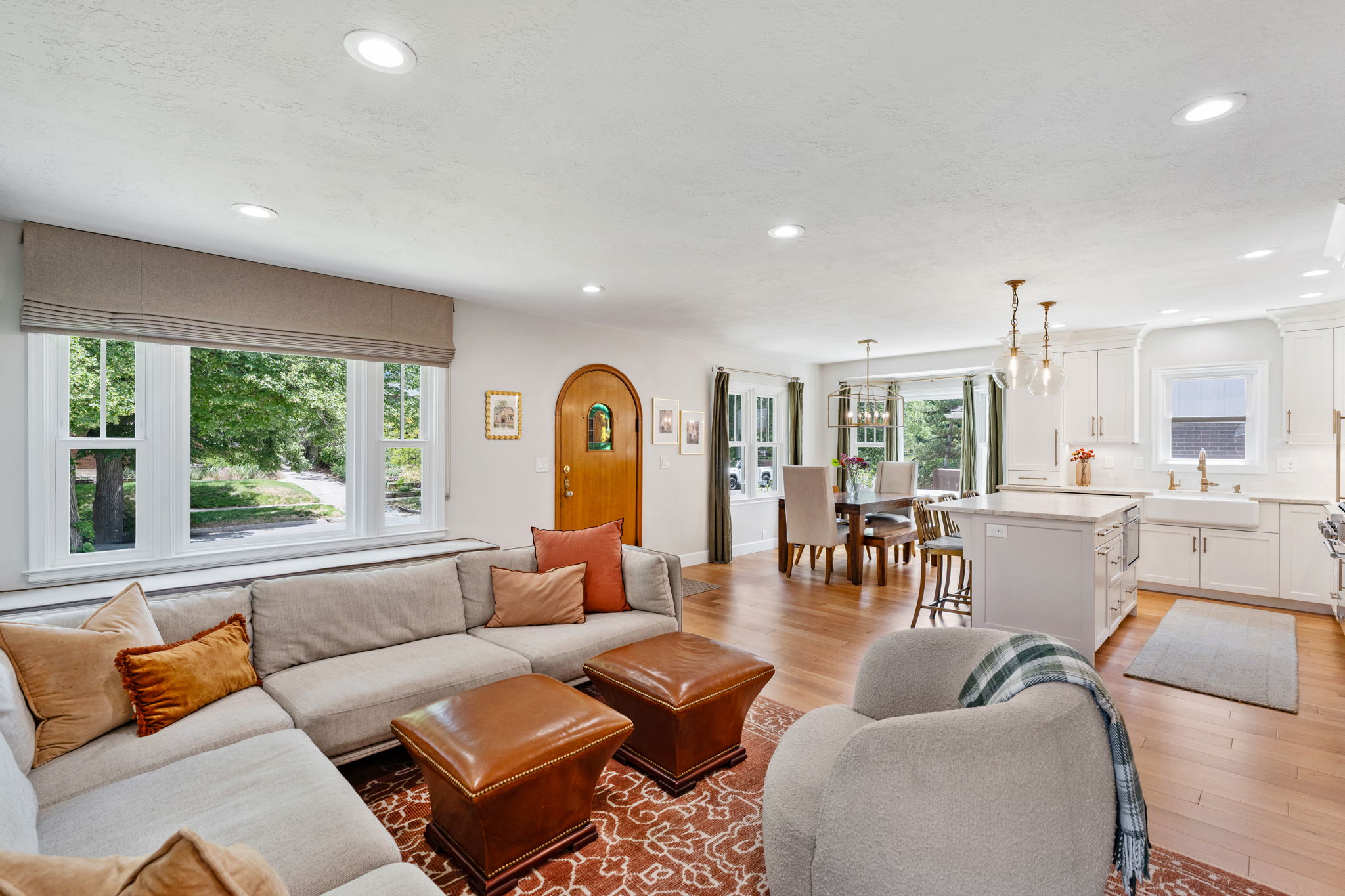 Open-concept living space featuring wood-finish flooring, recessed lighting, a modern kitchen with white cabinetry, a central island with bar seating, and a dining area