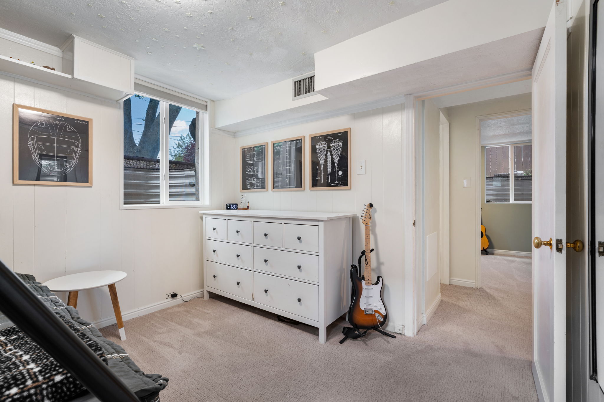 Carpeted room featuring a double-hung window, white paneled walls, and a white six-drawer dresser with dark hardware