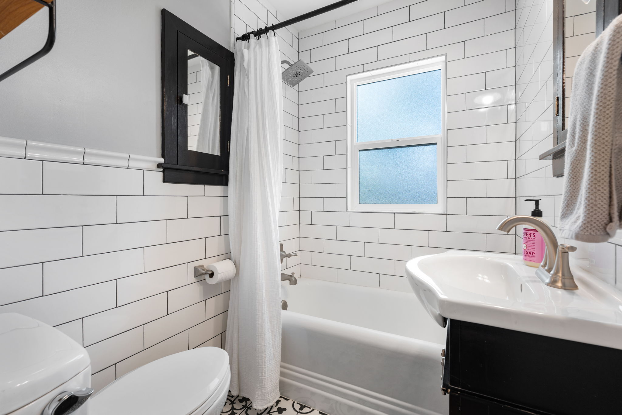 Bathroom featuring white subway tile walls, a built-in tub with shower, and a pedestal sink with brushed nickel faucet