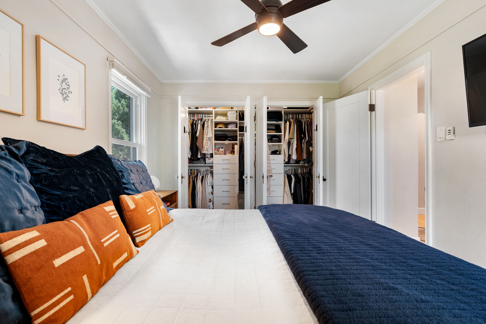 Bedroom featuring two integrated closets with custom shelving and drawer systems, a ceiling fan, crown molding, and a window providing natural light