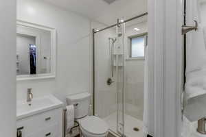 Bright bathroom featuring a glass-enclosed shower with built-in shelving, white vanity with integrated sink, brushed nickel fixtures, and a framed mirror
