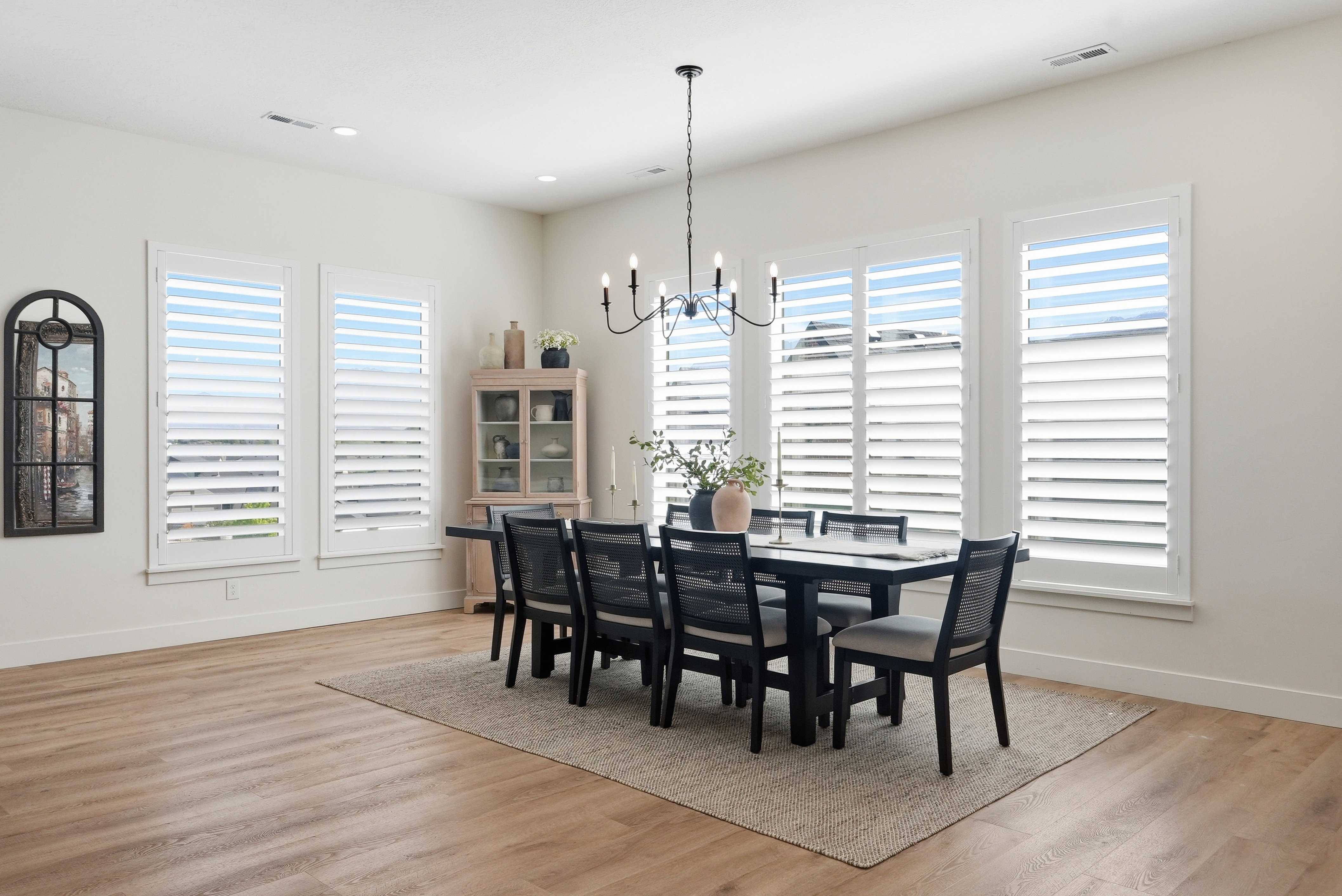 Spacious dining area featuring large windows with plantation shutters, LVP flooring, a contemporary chandelier, and a neutral wall palette