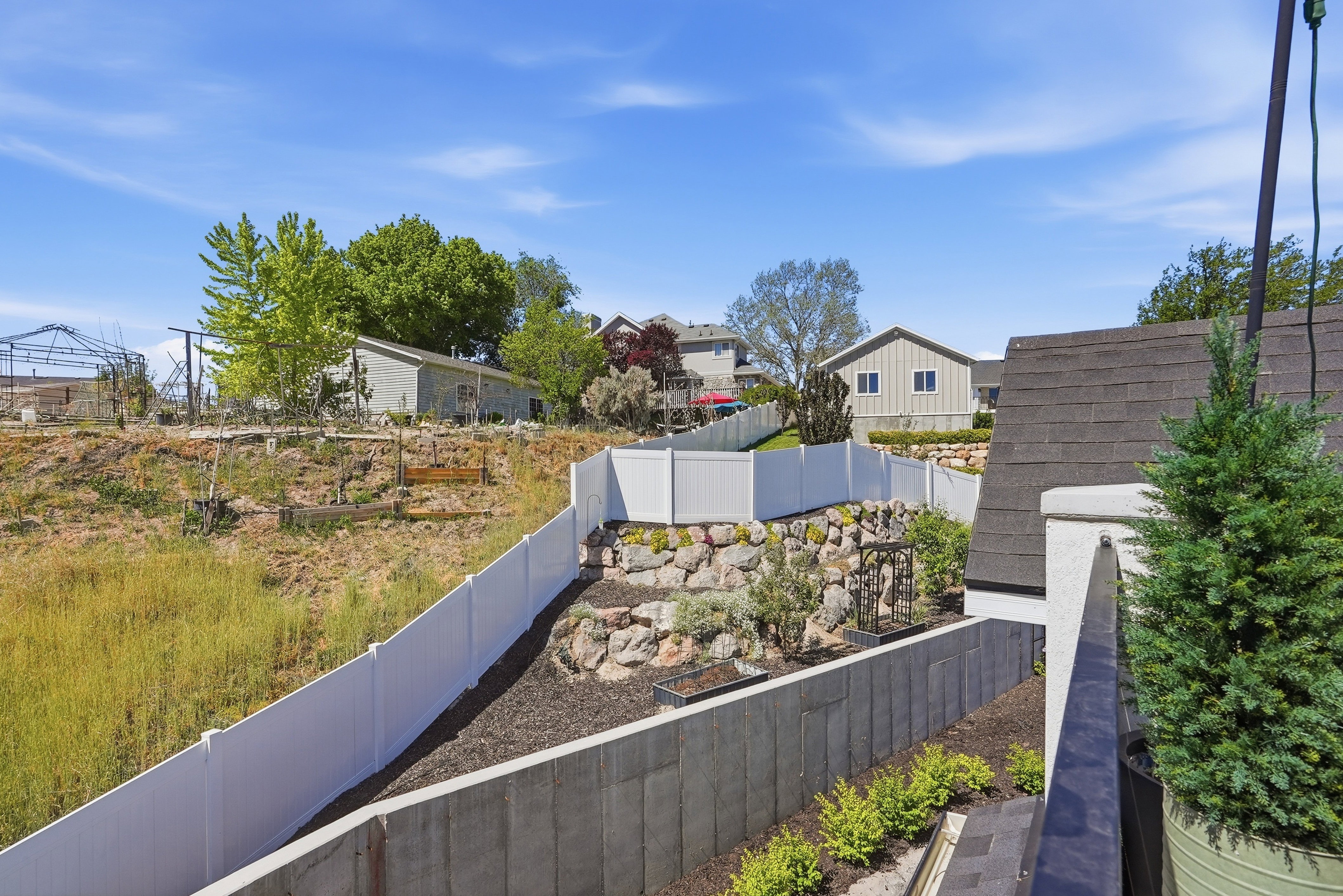 Terraced landscaping featuring a white vinyl privacy fence, rock retaining wall, and planted shrubs