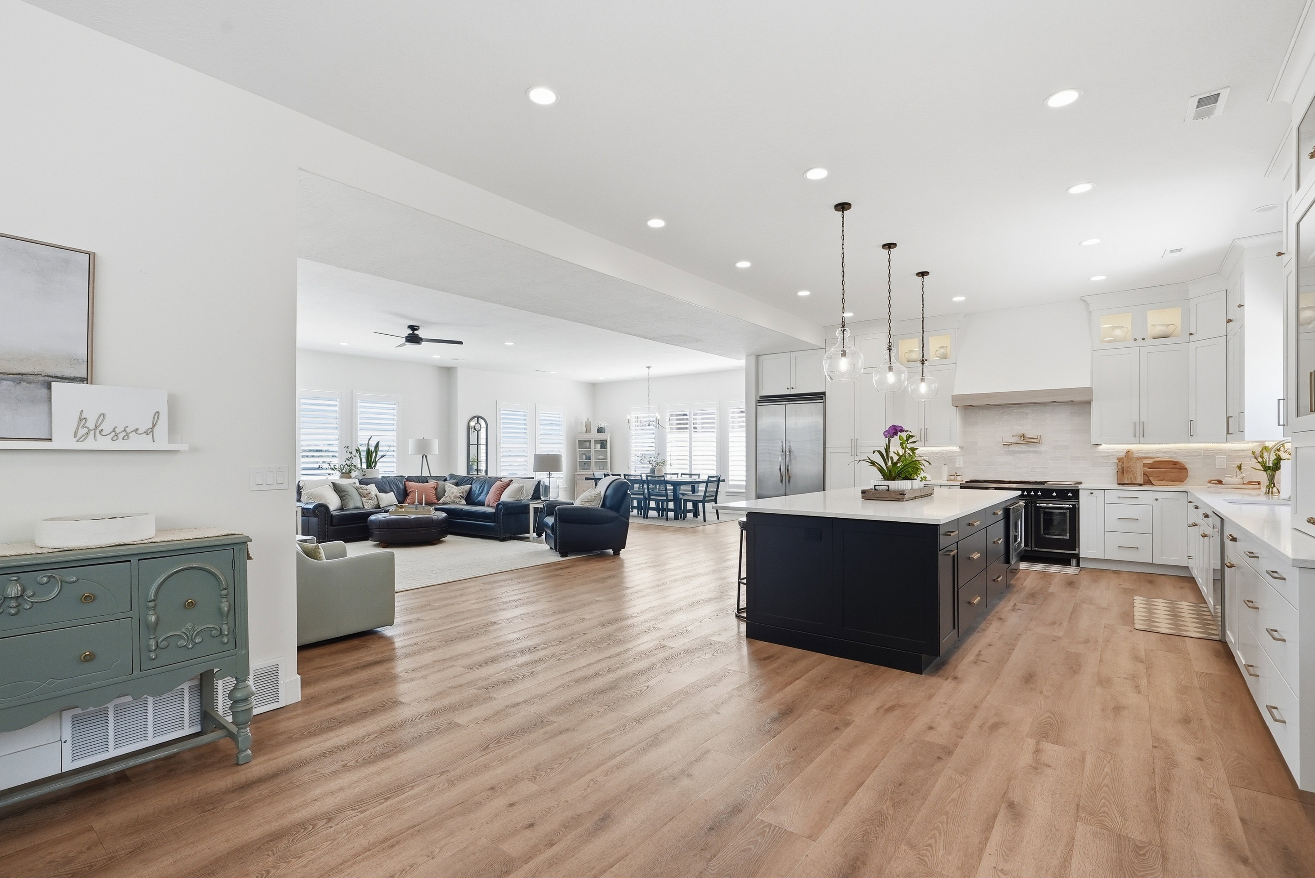 Open-concept living space featuring wood-finish flooring, a contemporary kitchen with a dark-toned island and light-toned cabinetry, stainless steel appliances, and recessed lighting
