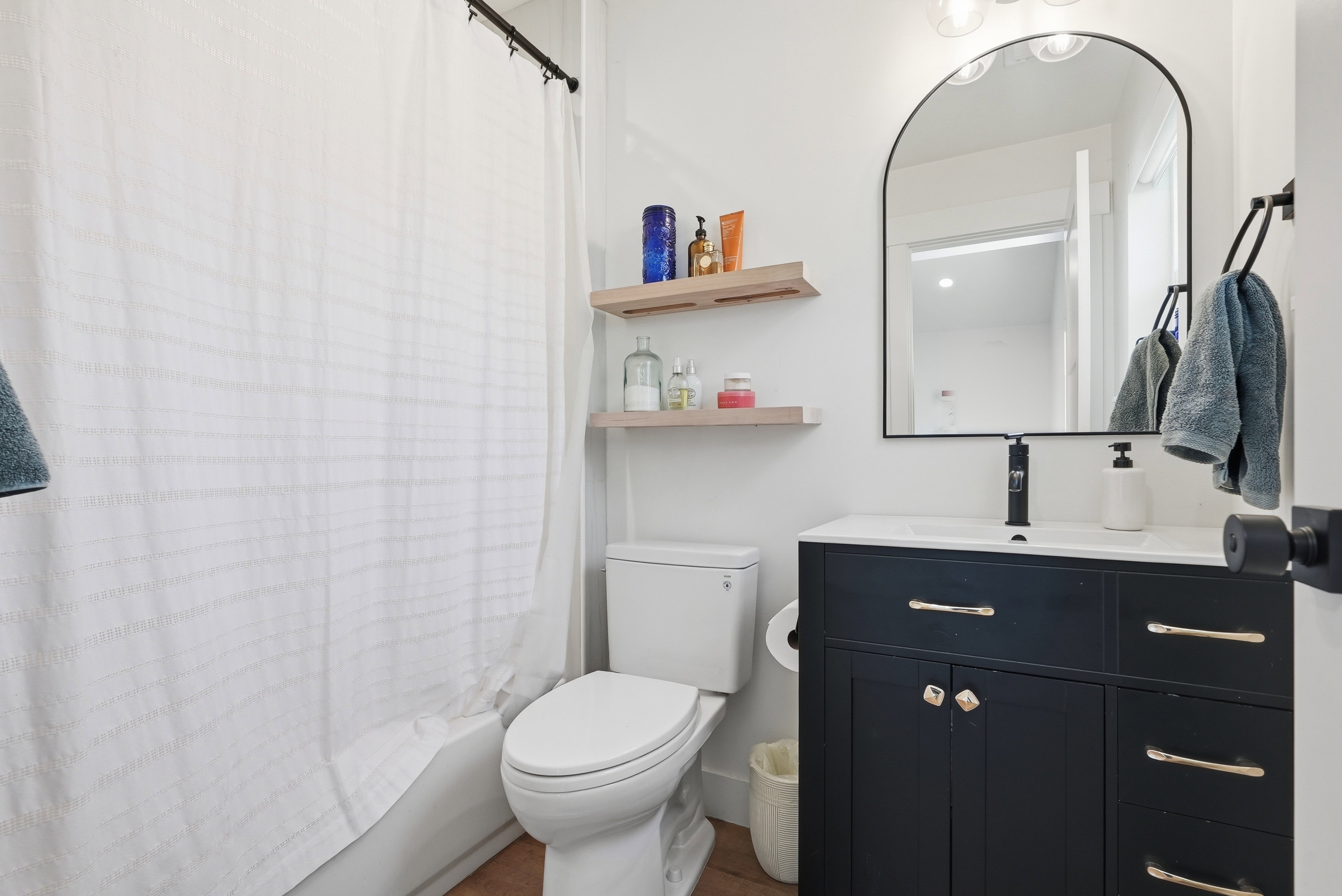 Bathroom featuring a dark vanity with gold hardware, a white integrated sink, and a black wall-mounted faucet