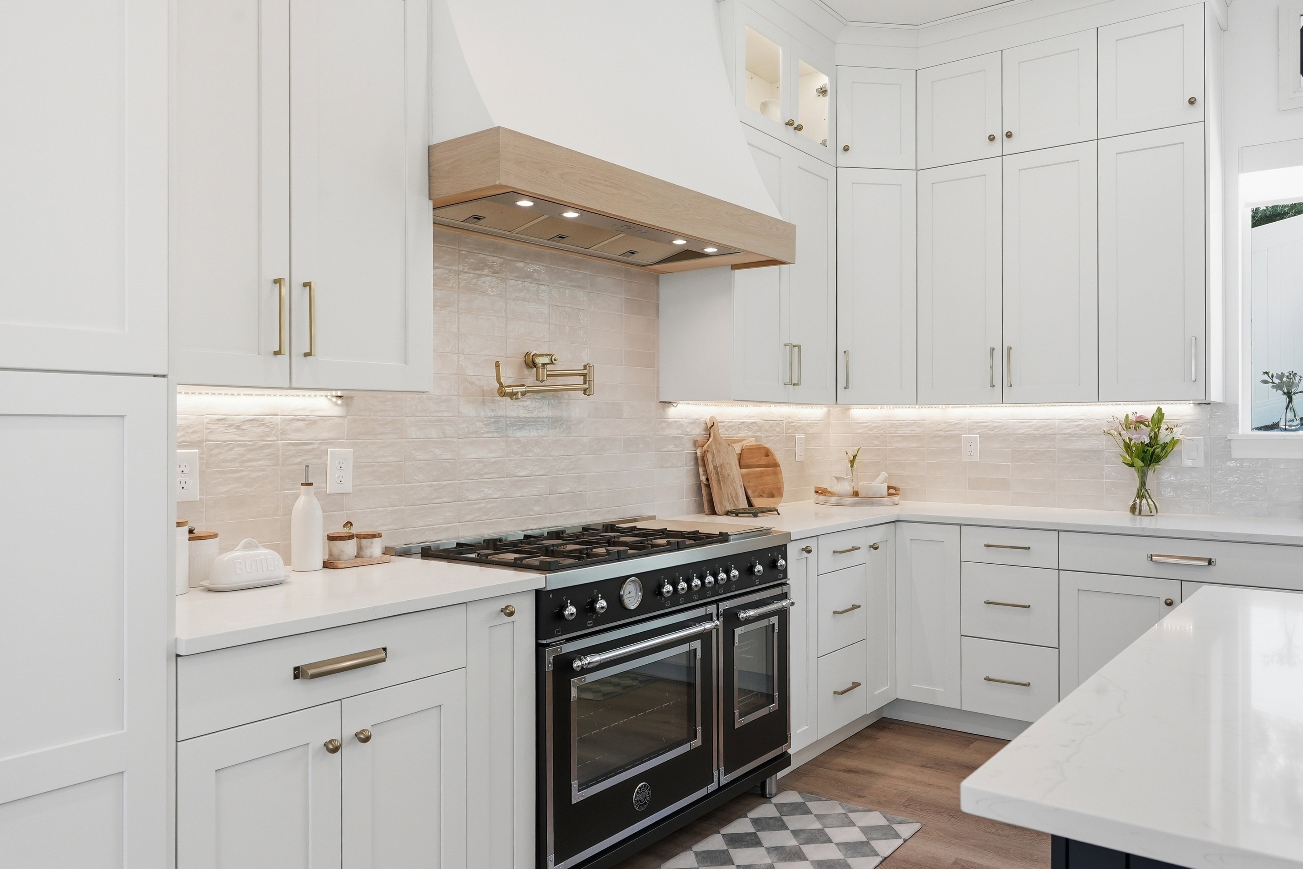 Gourmet kitchen featuring a professional-grade range, pot filler, shaker cabinetry with brass hardware, undermount lighting, and quartz countertops