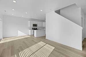 Open-concept living area with wood-finish flooring, recessed lighting, and a white kitchen featuring shaker cabinetry, an island, and stainless steel appliances