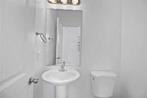 Pedestal sink with chrome faucet, a rectangular mirror, and a three-bulb vanity light fixture