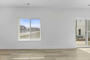 Open-concept living space with light wood-finish flooring, white walls, and a large window with horizontal blinds