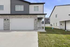 Modern townhome exterior featuring a two-car garage, stone veneer siding, fiber cement paneling, and a covered entryway