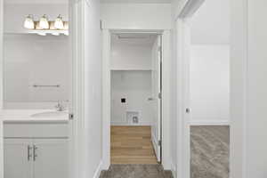 Hallway featuring neutral-toned carpeting, leading to a utility space with wood-finish flooring and a white built-in shelf
