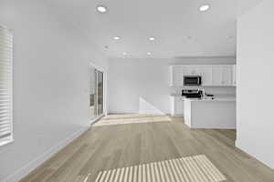 Open-concept living area featuring light wood-finish flooring, recessed ceiling lighting, and crisp white walls