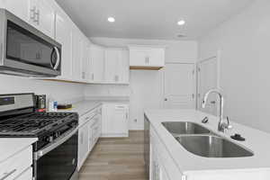 Kitchen featuring white cabinetry with silver hardware, light-toned wood-finish flooring, and white countertops