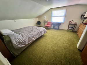 Room with textured green carpeting, sloped ceilings, and a window with blinds