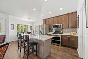 Kitchen with stainless steel appliances, backsplash, lofted ceiling, dark wood-style floors, and a kitchen bar
