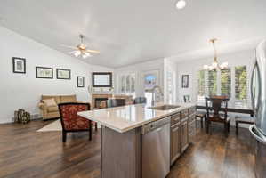 Kitchen with light stone counters, lofted ceiling, appliances with stainless steel finishes, an island with sink, and decorative light fixtures